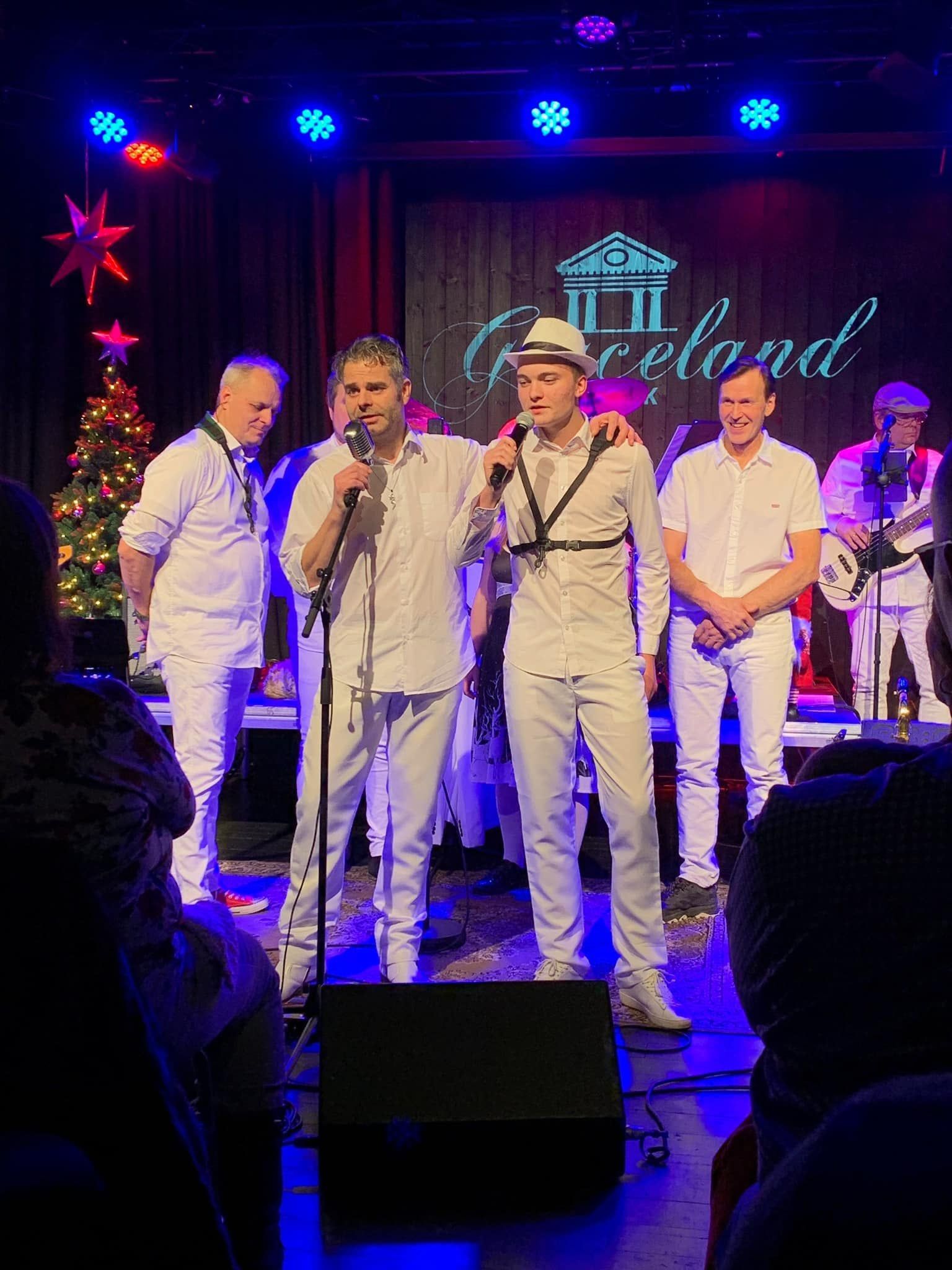 Morten Arnesen og Nicklas Arnesen synger sammen på scenen under en julekonsert, med juletre og Graceland-logo i bakgrunnen